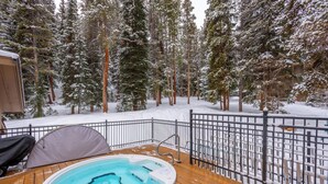 An outdoor hot tub on a wooden deck with a metal railing, surrounded by snow-covered trees. - Nice Ski-in/Walk-out condo, free wifi, & parking. (Copper Mountain)