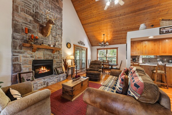 Una sala de estar acogedora con chimenea de piedra, asientos cómodos y una cocina al fondo.