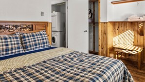Un dormitorio con cama, cabecera de madera, lavadora y una silla de madera.