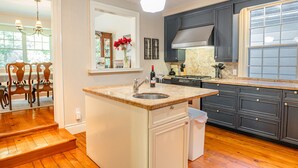 A kitchen with a central island, dark cabinets, a window, and a dining area with wooden chairs. - Arbour House, 1830 Historic Home (Niagara-on-the-Lake)