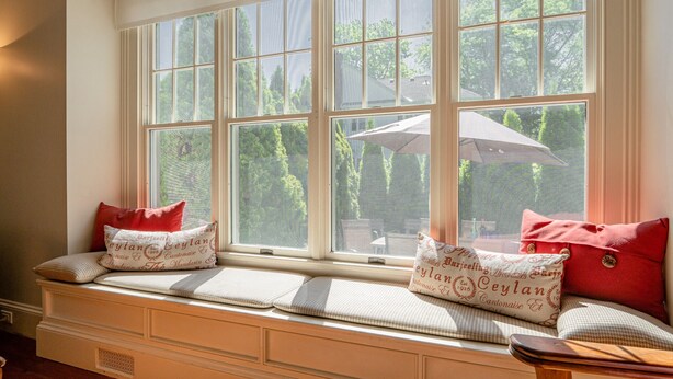 A bay window with multiple panes, a bench with cushions, and a view of greenery outside. - Arbour House, 1830 Historic Home (Niagara-on-the-Lake)