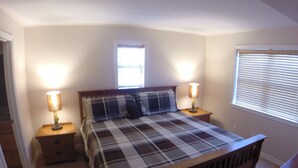 Une chambre à coucher avec un lit, deux lampes de chevet, une fenêtre avec des stores et une petite fenêtre située au-dessus du lit.