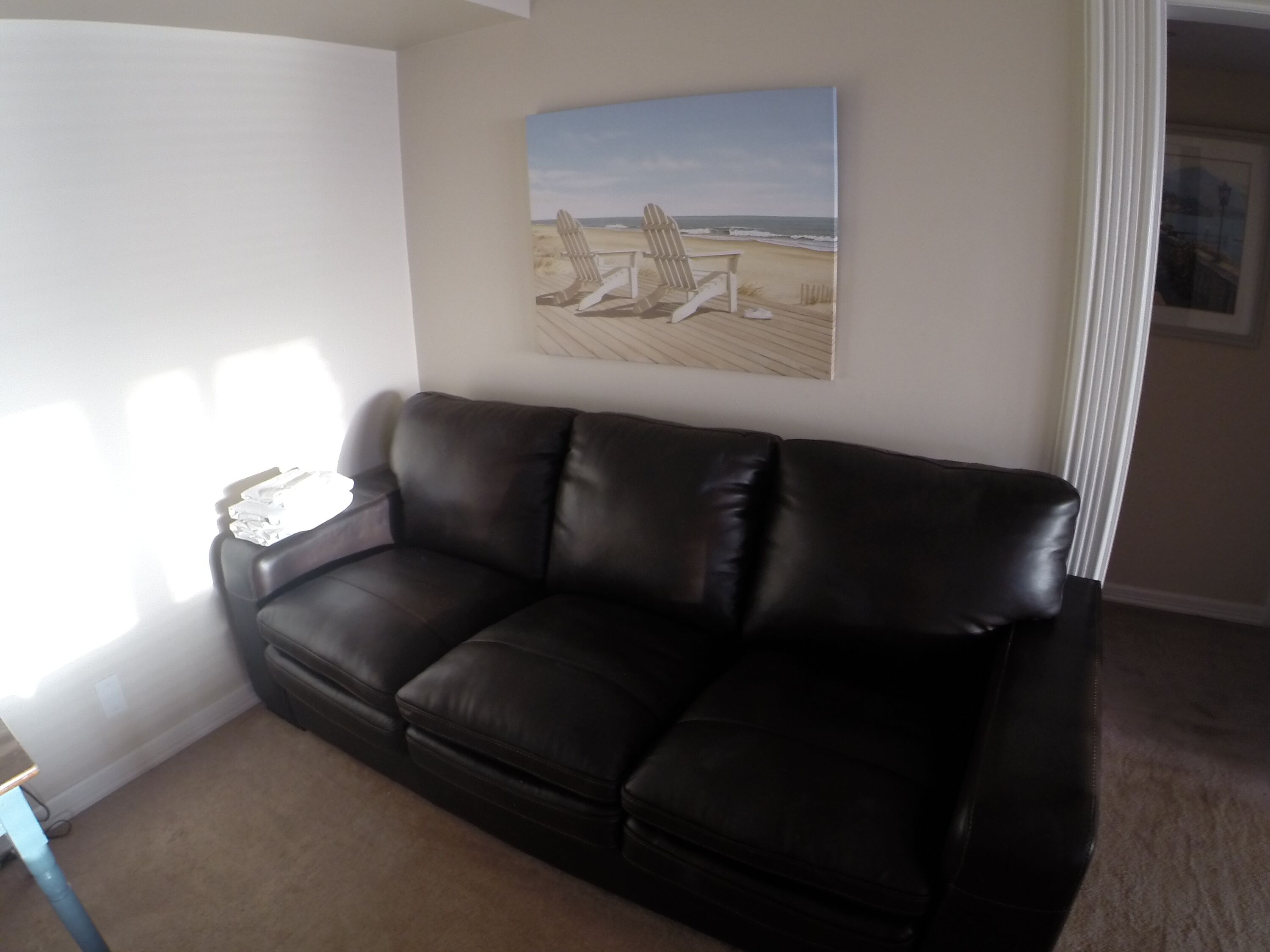 Un canapé en cuir marron foncé dans un salon, avec un tableau représentant une scène de plage accroché au mur.