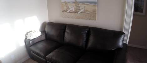 Un canapé en cuir marron foncé dans un salon, avec un tableau représentant une scène de plage accroché au mur.