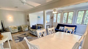 A spacious living room with a large dining table, two sofas, and a ceiling fan. - Kith And Kin:  Old Ocracoke style cottage, spacious screened porch. (Ocracoke)