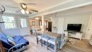 A spacious living area with a dining table, a sofa, and a TV. - Kith And Kin:  Old Ocracoke style cottage, spacious screened porch. (Ocracoke)