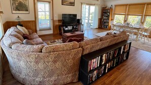 Ein Wohnzimmer mit Ecksofa, Fernseher, Bücherregal und Essbereich mit Stühlen.