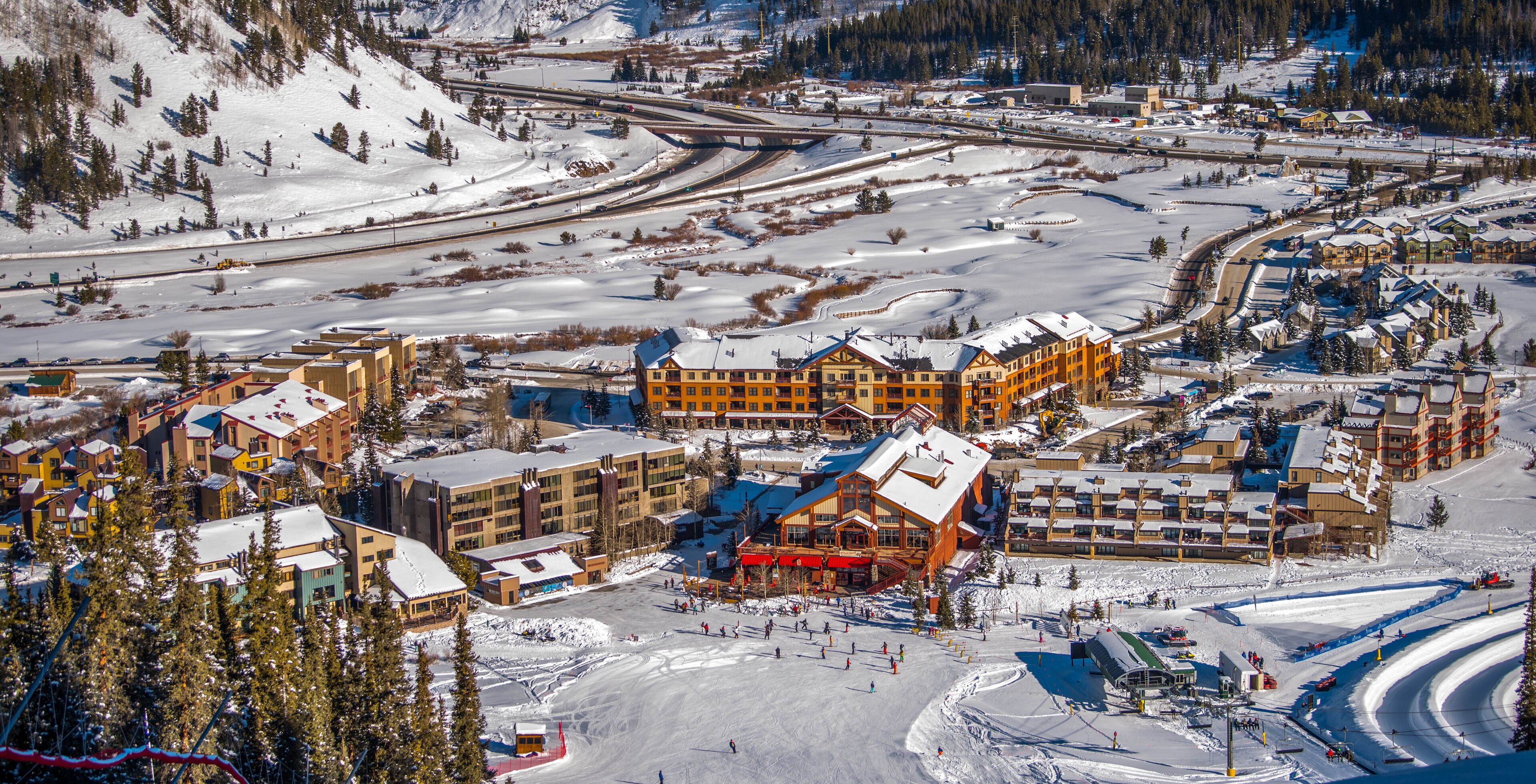 A ski resort with multiple buildings, including a large lodge and smaller cabins, surrounded by snowy terrain and ski slopes.