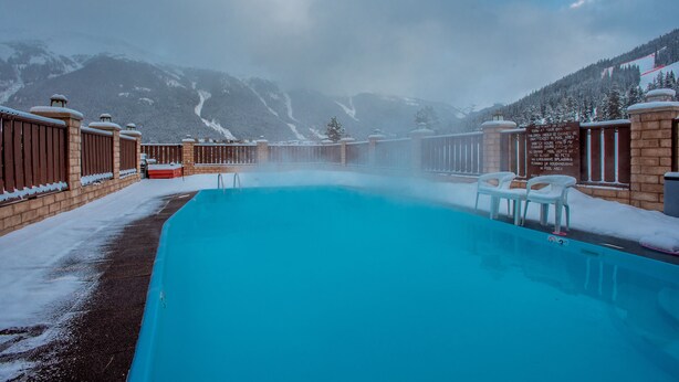 Una piscina con vista su montagne innevate e un'atmosfera nebbiosa.