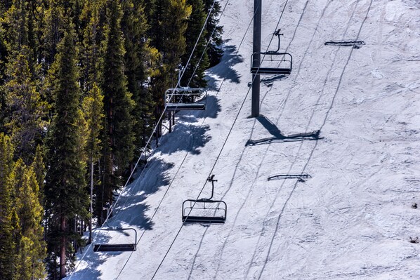 A ski lift with chairs moving along a snowy slope, surrounded by dense trees.