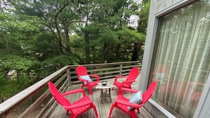 Una terraza de madera con cuatro sillas Adirondack rojas y una pequeña mesa, rodeada de árboles verdes y frondosos.