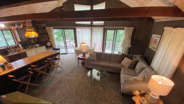 Una sala de estar acogedora con un sofá, una mesa de centro y una mesa de comedor con sillas. Amplias ventanas ofrecen luz natural y vistas al exterior.
