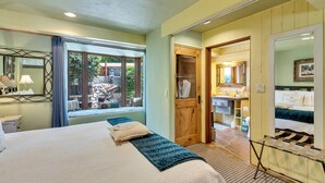 Une chambre avec un grand lit, une fenêtre donnant sur l’extérieur, une porte en bois et une salle de bain avec un miroir et un lavabo.