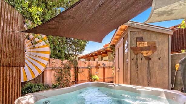 Un espace avec un jacuzzi, une terrasse en bois, un grand parasol et une clôture en bois.
