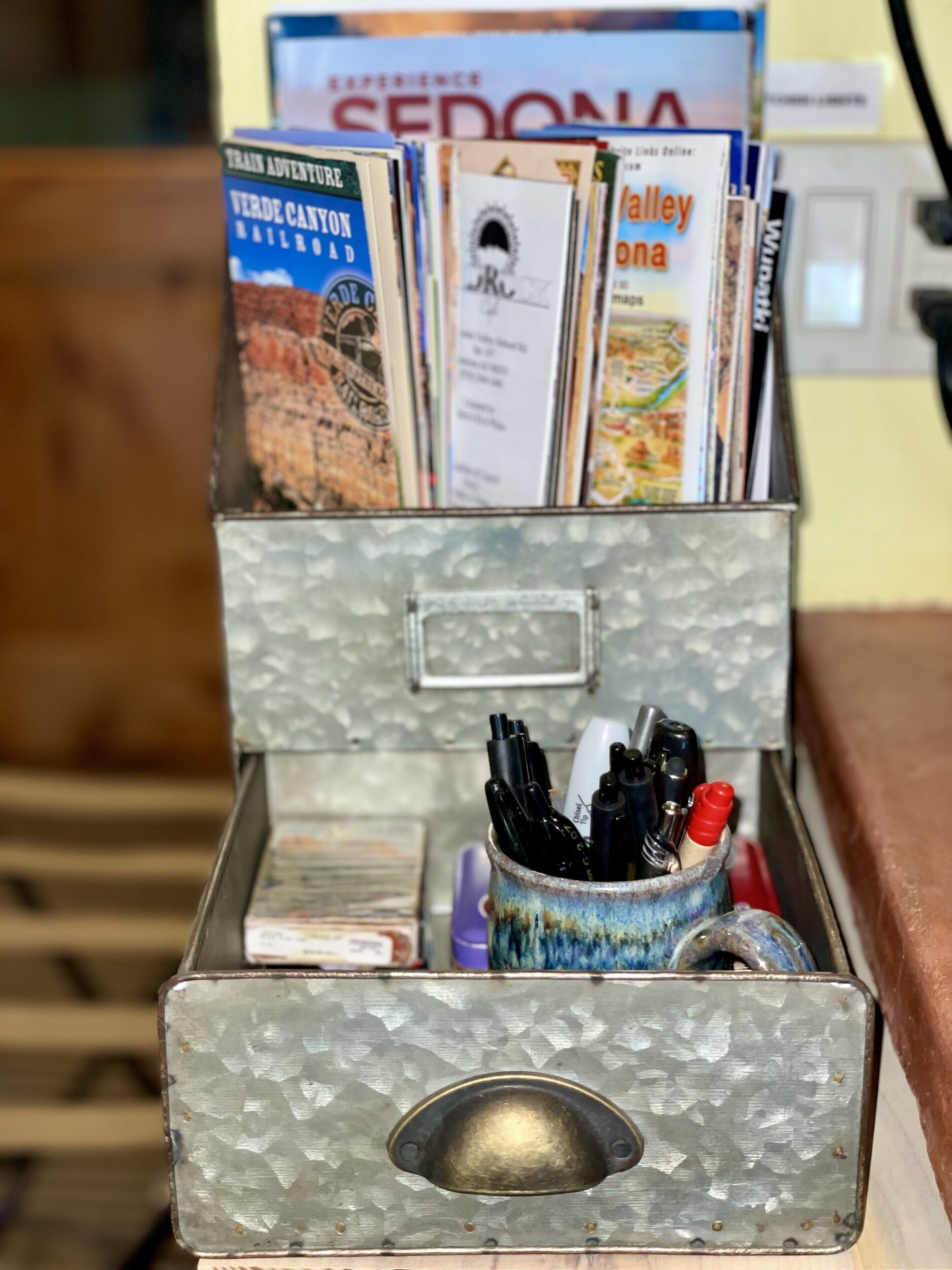 A metal box with a handle, containing various items including pens and a small container.