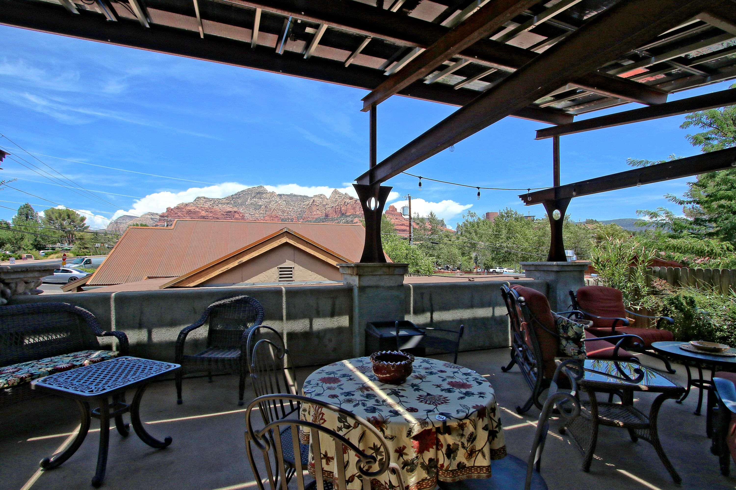 Une terrasse extérieure avec des meubles en osier, une table ronde recouverte d’une nappe à motifs floraux, et une vue sur les montagnes en arrière-plan.