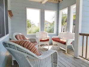 Une véranda avec des fauteuils et des coussins en osier, de grandes fenêtres et une terrasse en bois.