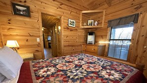 Ein Schlafzimmer einer Holzhütte mit einem großen Bett, einer gesteppten Decke, einem Schminktisch und einem Fernseher in der Ecke.