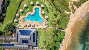 Vista aérea de un complejo turístico con piscina, playa y paneles solares en el edificio.