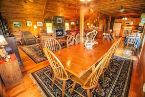 A wooden dining room with a large table and chairs, a fireplace, and a kitchen area with wooden cabinets and appliances. - 4th of July Still Avail!-4BR/4BA w/Hot Tub & Pool Table, Near West Jefferson (West Jefferson)