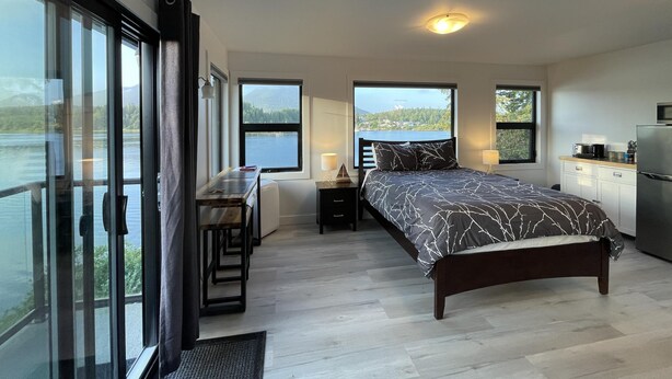 A bedroom with a bed, a desk, and a view of a lake. - Oceanfront Room with Hot Tub & Firepit (Ucluelet)