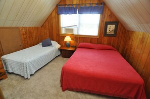 A small, cozy attic bedroom with two beds, a window with a view, and a lamp on a nightstand.