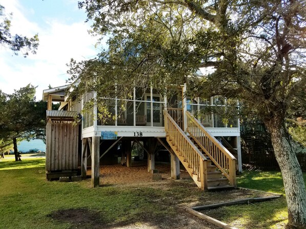 A wooden deck with a staircase leading to a covered area, surrounded by trees and a grassy area.