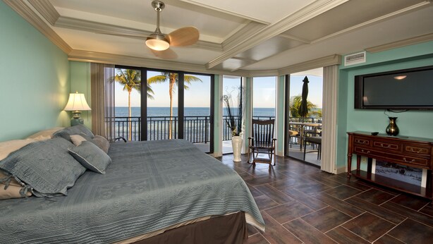 Ein geräumiges Schlafzimmer mit einem großen Bett, einem Balkon mit Meerblick und einem an der Wand montierten Fernseher.