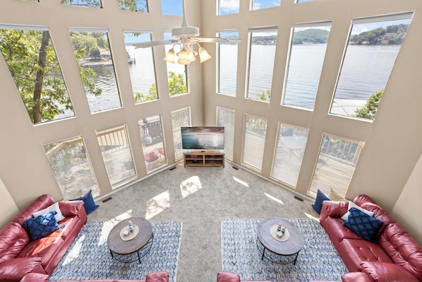 A room with large windows, a ceiling fan, a TV, and two sofas with a rug and coffee table.