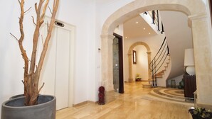 Eine geräumige Lobby mit Marmorboden, einer Treppe mit schmiedeeisernem Geländer und einem großen Kübelbaum.