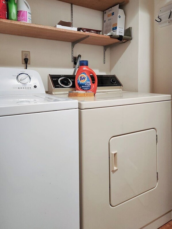 Un espace buanderie comprenant un lave-linge, un sèche-linge et une étagère où sont rangés les produits de nettoyage.