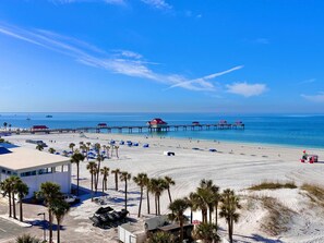 Ein Strand mit einer Promenade, Palmen und Strandsonnenschirmen.