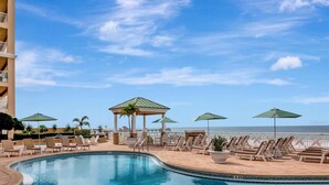 A pool area with lounge chairs and umbrellas, a gazebo, and a view of the ocean.
