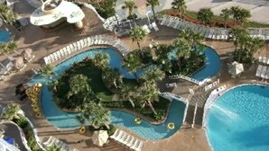 An aerial view of a resort with multiple swimming pools, palm trees, and lounge areas.