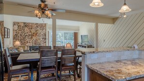 A dining area with a stone wall, wooden furniture, and a ceiling fan. - Ridge Condo 2672 - Upgraded With Great Views and Elkhorn Resort Amenities (Elkhorn)