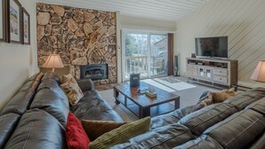 A living room with a stone wall, leather sofas, a fireplace, and a television. - Ridge Condo 2672 - Upgraded With Great Views and Elkhorn Resort Amenities (Elkhorn)