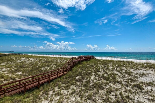 Un muelle de madera que conduce a una playa, con un cielo azul despejado y el océano al fondo.