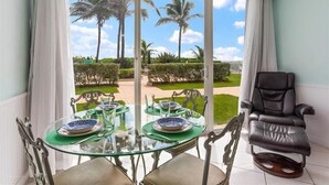Un espace repas avec une table en verre, des chaises et une vue sur des palmiers et un jardin.
