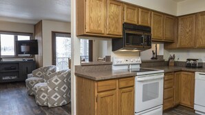 A modern kitchen with wooden cabinets, a microwave, stove, and a dining area with a TV and seating. - Bright, Modern On-Mountain Condo (Whitefish)