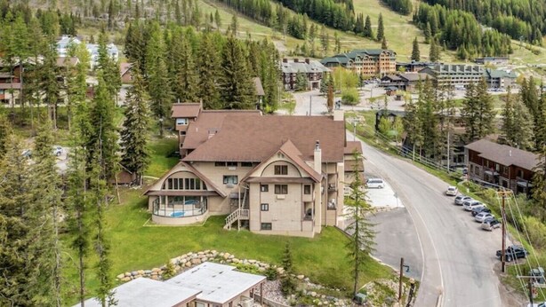 A large, two-story building with a prominent front porch and a driveway leading to a parking area. - Bright, Modern On-Mountain Condo (Whitefish)