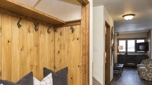 A wooden bench with pillows, a kitchen area with a TV, and a patterned sofa. - Bright, Modern On-Mountain Condo (Whitefish)