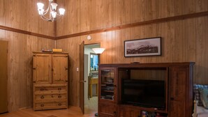 Uma sala de estar com painéis de madeira, televisão, armário de madeira e um candelabro.