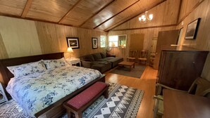 Um quarto aconchegante com uma cama grande, um banquinho de madeira, uma mesinha e um sofá.