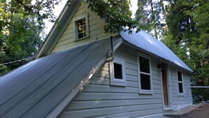 Uma pequena casa térrea com telhado triangular e varanda frontal.
