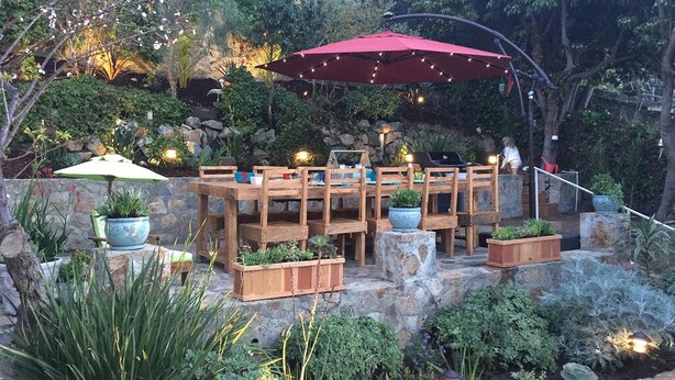 Eine Terrasse im Freien mit Holztischen und -stühlen, umgeben von Steinmauern und Topfpflanzen.