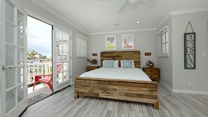 Ein Schlafzimmer mit einem hölzernen Bett, weißen Wänden und einem Balkon mit einem roten Stuhl.