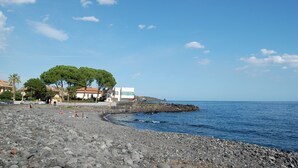 A rocky beach with a few buildings and trees in the background. - Three room apartment :Seafront residence with pool and garden (Santa Tecla di Acireale)