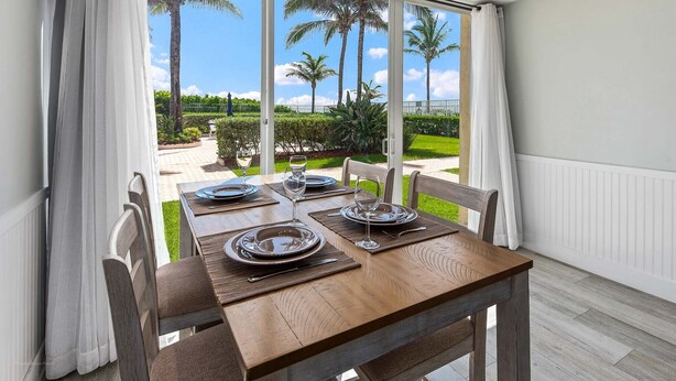 A dining table set for four with a view of palm trees and a garden.