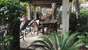 Patio esterno con tavoli e sedie in legno, immerso nel verde e palme.