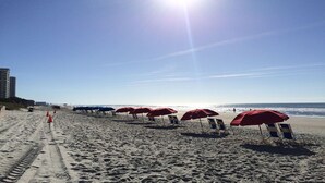 Una spiaggia con file di ombrelloni rossi e lettini, cielo sereno e l'oceano sullo sfondo.